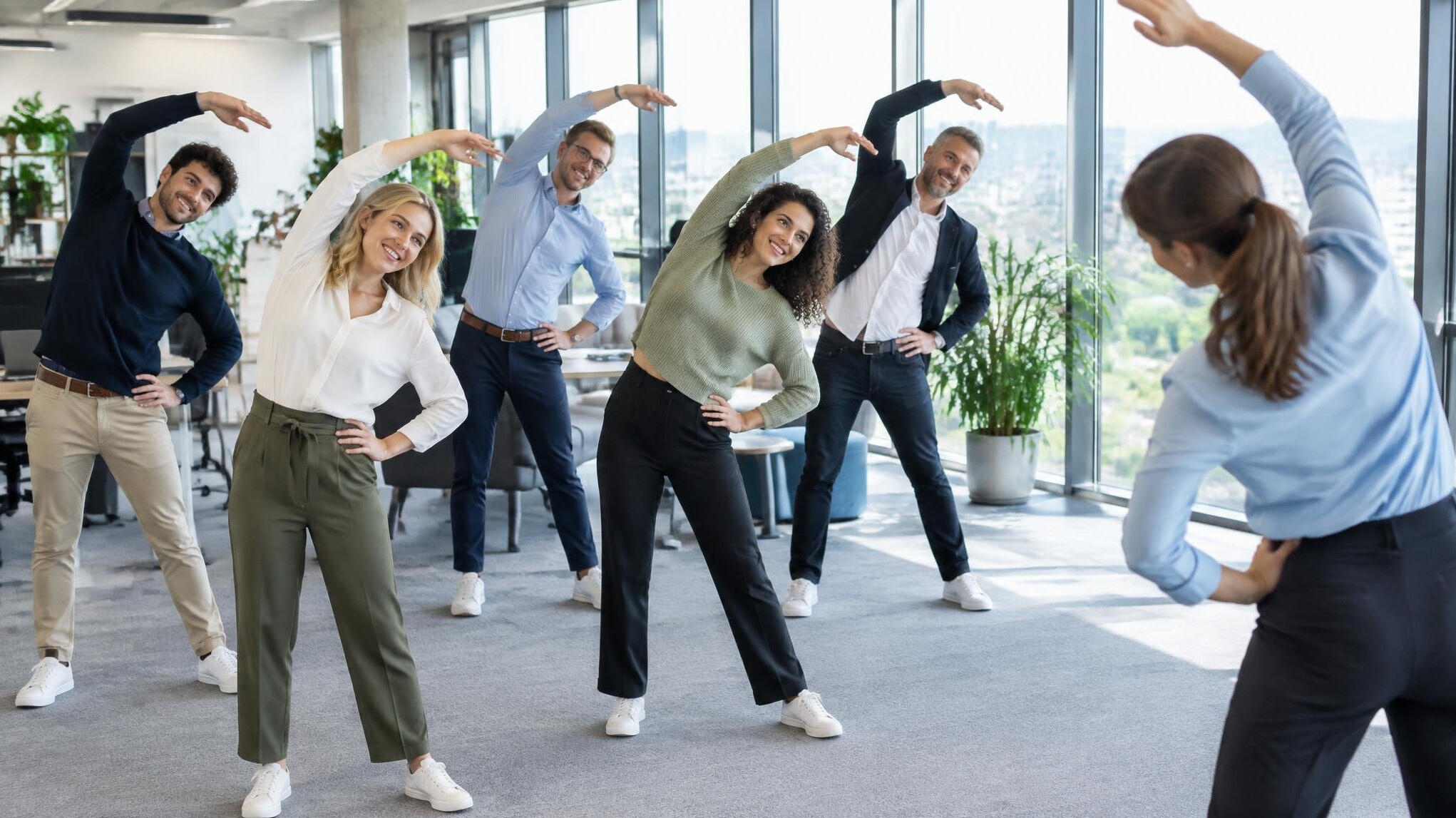 Group of coworkers doing a guided stretching exercise in an office